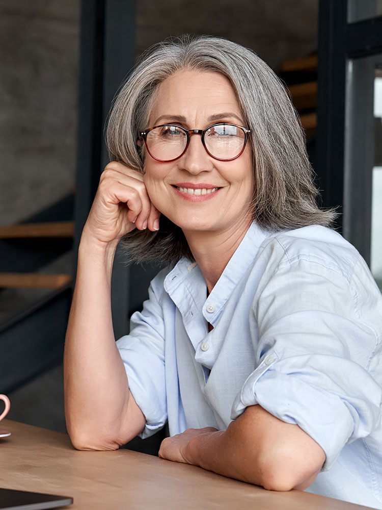 Headshot of a middle aged woman in glasses happily leaning over a coffee counter